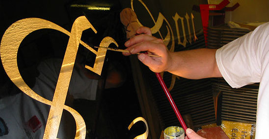 Glass sign being hand painted and guilded with gold leaf.